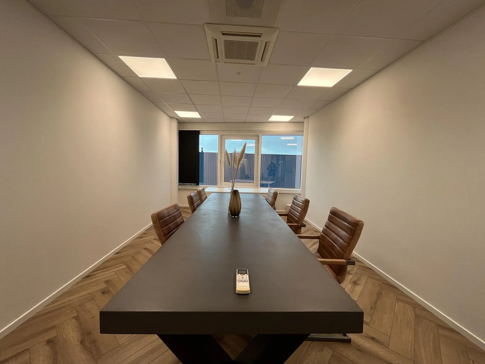 Vergaderruimte aan de Lange Dreef met een lange zwarte tafel, zes leren stoelen en een vaas met decoratie.